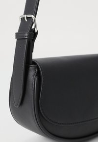 Schwarze Leder-Umhängetasche mit einer geschwungenen Form, ausgestattet mit einer silbernen Metallschnalle an einem Riemen und minimalistischen Stickdetails.