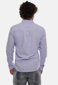 Camisa de manga larga azul claro con cuello abotonado, pliegue en la espalda y puños con botón. Confeccionada en tejido de algodón, de textura suave.
