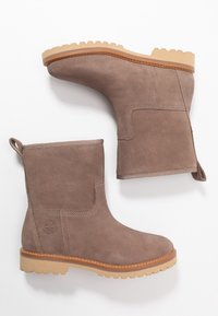 Bottines en daim marron avec une semelle épaisse en caoutchouc marron clair, dotées d'un embout arrondi, de panneaux élastiques latéraux et d'une petite languette à l'arrière.