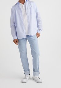 Ljusblårandig långärmad skjorta över en vit polo, i kombination med ljusa jeans och vita sneakers. Knappneddesign med bröstficka.