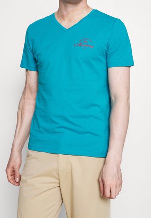 Türkisfarbenes V-Ausschnitt-T-Shirt aus Baumwolle. Verfügt über ein kleines rotes Grafiklogo auf der Brust. Glatte Textur, kurze Ärmel und lockere Passform.