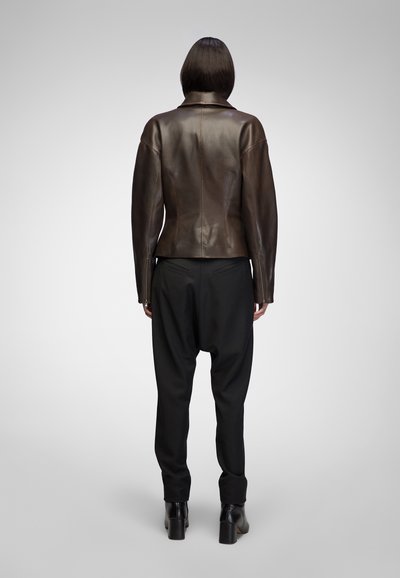 Brown leather jacket with a fitted design, featuring a stand-up collar and seam detailing, paired with black loose-fitting pants and heeled boots.