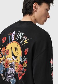 Camisa negra de manga larga con un diseño gráfico colorido que incluye flores, una cara sonriente y varios personajes en la parte trasera.