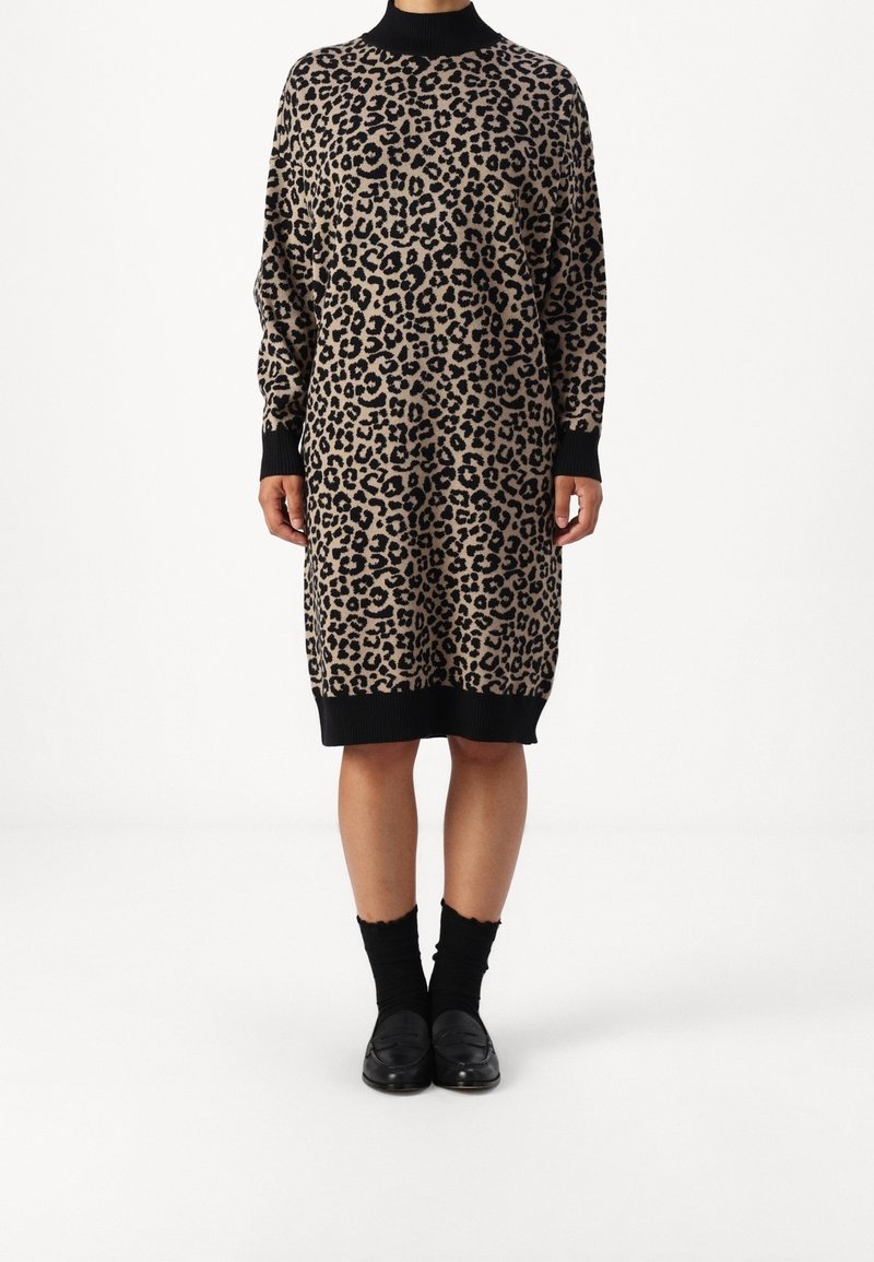 Robe tricotée à imprimé léopard avec un col montant, des manches longues, et des poignets et un ourlet côtelés noirs contrastants. Portée avec des mocassins noirs et des chaussettes.