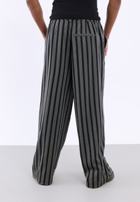 Pantaloni largi cu dungi negre și gri, cu talie elastică și o buzunare pe spate. Textură netedă și croială lejeră pentru confort.