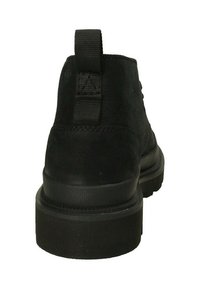 Stivaletti neri in suede con suola nera spessa. Presentano un'impugnatura a cappio sul tallone e dettagli cuciti sul retro. Texture liscia.