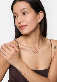 Set di gioielli in oro rosa composto da orecchini a forma di cuore, una collana coordinata e un bracciale. Finitura metallica liscia con eleganti design a catena.