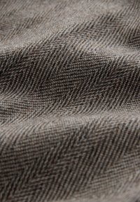 Tkanina w wzór jodełki w odcieniach brązu i szarości, charakteryzująca się miękką fakturą i subtelnym połyskiem. Falejące fałdy tworzą głębię.