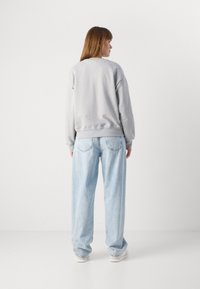 Felpa grigia con colletto a girocollo, vestibilità comoda e polsini a costine, abbinata a jeans a gamba larga di un blu chiaro e sneakers bianche.