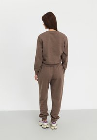 Ensemble de sweatshirt en coton marron et de joggings avec des poignets et une taille côtelés ; associé à des baskets multicolores, vu de dos.