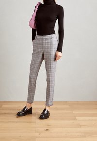 Černý rolák, šedé kalhoty s kostkovaným vzorem a černé mokasíny. Kalhoty mají přiléhavý střih s jemnými barevnými liniemi ve vzoru. Růžová kabelka jako akcent.