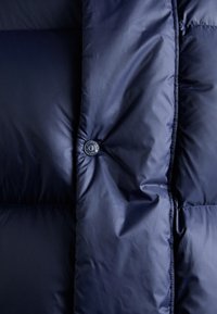 Κοντινό πλάνο ενός ναυτικού μπλε πονταριστού μπουφάν με κούμπωμα με κουμπιά σsnap και λεπτομέρειες από επενδεδυμένη ραφή.