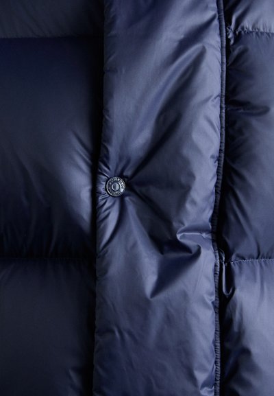 Nahaufnahme einer marineblauen gesteppte Jacke mit Druckknopfverschluss und gepolsterten Steppdetails.
