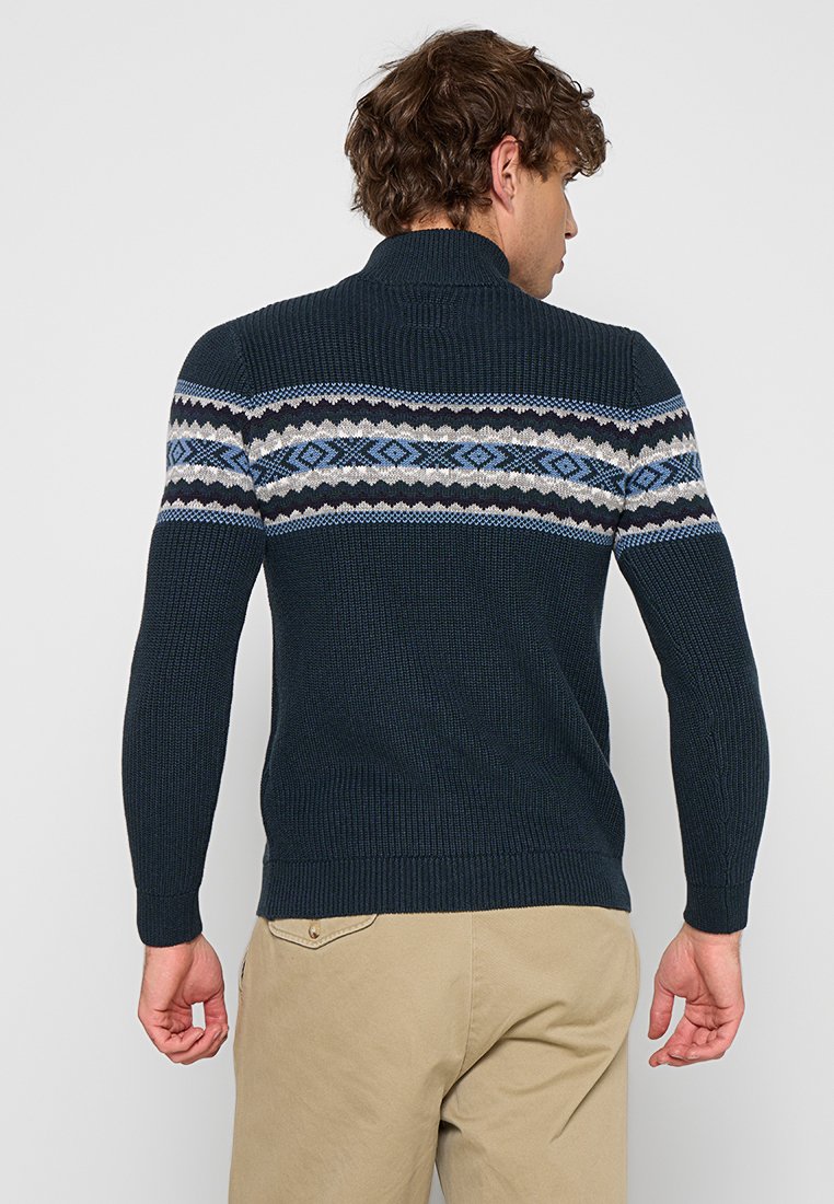 Marineblauwe gebreide trui met een gestreepte horizontale band in blauw, grijs en wit. Voorzien van een hoge hals en geribbelde manchetten en zoom.