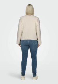 Pull en polaire beige avec des épaules tombantes, un tissu texturé et une coupe courte, associé à un jean skinny bleu et des chaussures beiges.