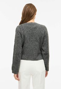 Pilkas trumpintas megztinis iš tekstūruoto mezgimo, ilgomis rankovėmis ir apvaliu kaklu, derinamas su baltomis aukštakulnėmis kelnėmis.