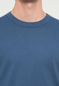 Niebieski sweter dziany z fakturą prążkowaną, z okrągłym dekoltem i krótkimi rękawami, prezentujący jednolity kolor bez wzorów czy ozdób.