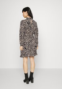 Vestido com padrão de zebra em tons de castanho e preto, com cintura ajustada, mangas longas, bainha franzida e detalhe nas costas em forma de coração. Usado com botas pretas de cano curto.
