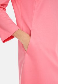 Roze jurk stof met een gladde textuur, met 3/4 mouwen en een zijzak geïntegreerd in het ontwerp.