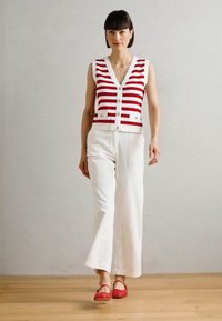 Pantalones anchos blancos combinados con una blusa sin mangas a rayas rojas y blancas con botones. Llevados con zapatos planos rojos. Textura suave, diseño casual.