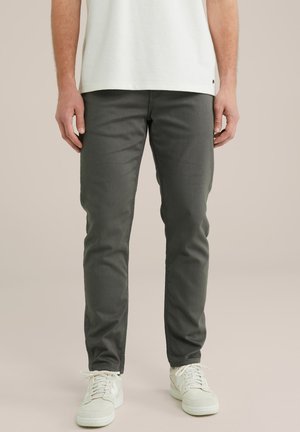 Dunkelgraue Slim-Fit-Jeans aus Baumwollmischung, die eine glatte Textur und subtile Nähte aufweisen. Kombiniert mit weißen Turnschuhen.