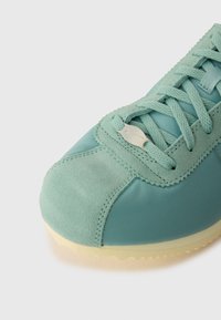 Svijetloplave tenisice sa gornjim dijelom od suede i najlona, teksturiranim vezicama, srebrnim metalnim detaljem i kontrastnom žutom potplatu.