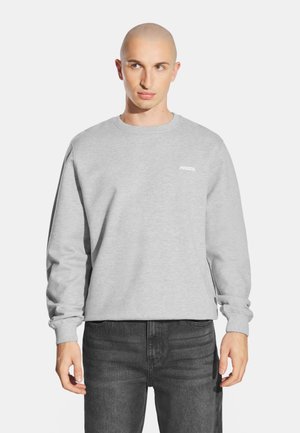 Szary sweter typu crewneck wykonany z miękkiego materiału, z małym białym logo "PROSTO." na lewym piersi oraz elastycznymi mankietami.