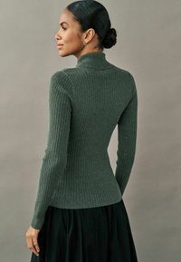 Rippstrick-Turtleneck-Pullover in Dunkelgrün, figurbetonter Schnitt, lange Ärmel, strukturierter Stoff, kombiniert mit einem schwarzen Rock.