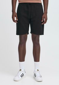 Zwarte katoenen shorts met een elastische tailleband en aansnoerkoord, met een eenvoudig ontwerp en rechte snit, gedragen met witte sneakers en sokken.