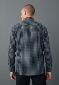Camicia a quadri nera e blu, con bottoni, maniche lunghe, tessuto strutturato e colletto standard, vista da dietro.