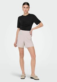 Top negro de manga corta con fruncido en la parte delantera y pantalones cortos de cintura alta en beige claro con botones laterales. Combinado con mocasines claros.