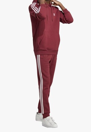 Burgundowa bluza z kapturem z białymi paskami na rękawach, kieszeń kangurza i dopasowane burgundowe spodnie z bocznym paskiem, współgrające z białymi sneakersami.