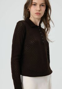 Bruine gebreide trui met een ruitpatroon, kraag en schouderbies met zes knopen. Voorzien van lange mouwen en een gestructureerd ontwerp.