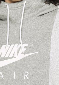 Šedá mikina s vysokým límcem, bílými tkaničkami a velkým bílým logem "NIKE AIR" na přední straně. Textura látky vypadá jemně.