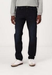 Mørkeblå denim jeans med rett passform, med frontlommer og knappelukking. Kombinert med hvite joggesko og en lys grå jakke.