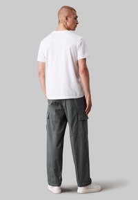 Wit T-shirt met korte mouwen, gecombineerd met grijze cargo broeken met zijzakken en een relaxed fit, aangevuld met witte sneakers.
