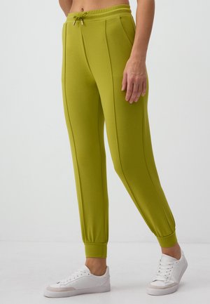 Jogging verde realizzati in tessuto morbido con vita regolabile, polsini affusolati e due cuciture laterali; abbinati a sneakers bianche.