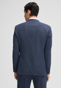 Giacca di abito blu navy sintonizzata con una trama testurizzata, rever a punta e maniche con quattro bottoni. La vista posteriore mostra una silhouette snella.