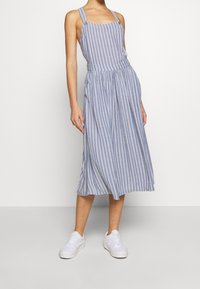Robe midi à rayures bleues et blanches avec bretelles réglables, taille élastique et coupe ample. Associée à des baskets blanches.