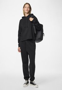 Μαύρο κοντό φούτερ με κορδόνια, συνδυασμένο με μαύρο παντελόνι τζόγκερ. Ολοκληρωμένη εμφάνιση με χαμηλά μαύρα και λευκά αθλητικά παπούτσια. Απλό σχέδιο.