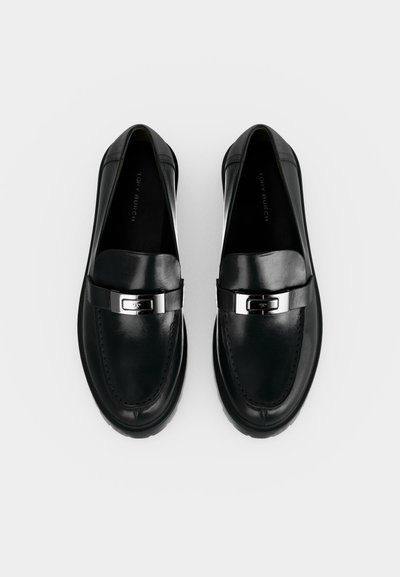 Ζευγάρι μαύρα δερμάτινα loafers με ασημένια μεταλλική αγκράφα, ορατή ραφή και στρογγυλεμένη μύτη, απεικονίζεται από πάνω σε λευκό φόντο.