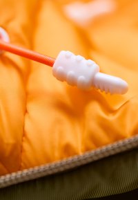 Pomarańczowy materiał o pikowanej teksturze, z białym plastikowym zapięciem z rowkami oraz przymocowanym pomarańczowym sznurkiem.