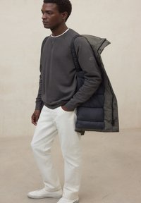 Felpa grigia con bordatura bianca sul collo, indossata sotto una giacca imbottita scura, abbinata a pantaloni bianchi e scarpe da ginnastica bianche. Design semplice e colori neutri.