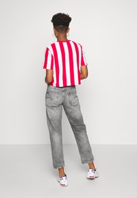 Camiseta recortada con rayas verticales rojas y blancas, combinada con vaqueros grises desgastados y zapatillas blancas con acentos coloridos.