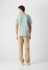 T-shirt de algodão verde claro com mangas curtas, conjugado com calças bege. O conjunto apresenta um corte descontraído e um design minimalista.
