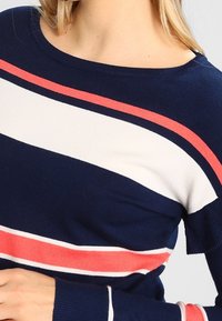 Marinblå stickad tröja med horisontella ränder i vitt och korall. Rund halsringning och ribbade ärmslut. Mjuk textur med en figurnära passform.