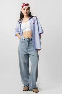Lichtblauwe oversized button-up shirt met een rode hartborduursel, witte crop top, relaxte lichtblauwe jeans en beige instap schoenen.