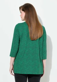 Zielona bluzka o liściastym wzorze, z rękawami do trzech ćwiartek i luźnym krojem. Materiał ma gładką strukturę.