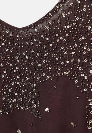 Dark purple fabric embellished with scattered black beads and silver sequins forming a textured, abstract pattern near a rounded neckline.