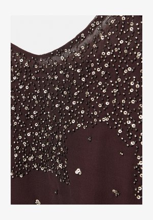 Tissu violet foncé orné de perles noires éparpillées et de sequins argentés formant un motif texturé et abstrait près d'un col arrondi.